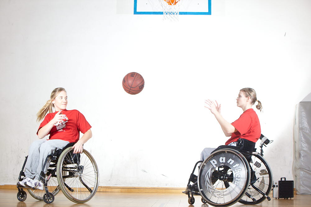 To som  sitter i en rullestol og kaster en basketball til hverandre